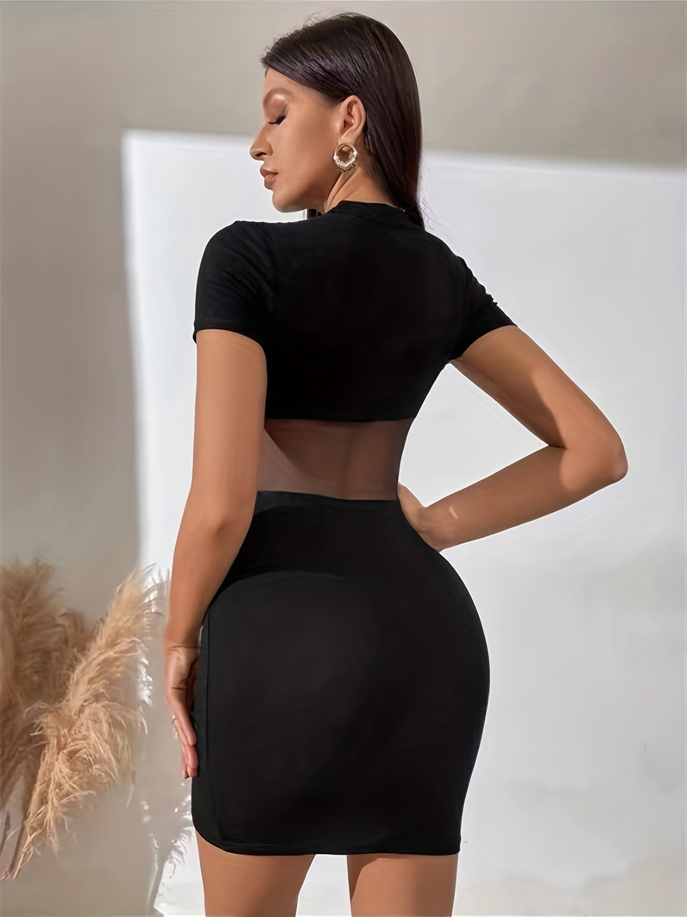 Woman wearing a black dress with a cutout back against a neutral background